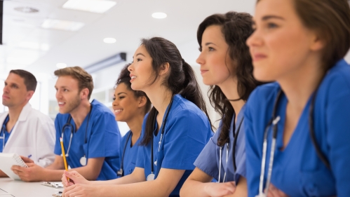 Medical school students wearing blue scrubs listen to a lecture