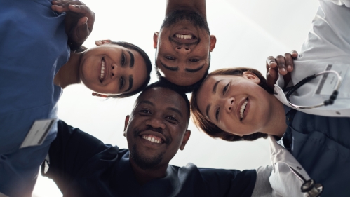 Four health care workers in a circle looking down at the camera 