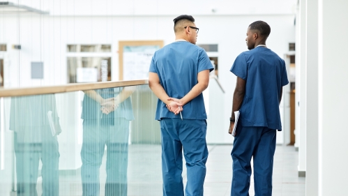 Two health care workers walk and talk in a hospital hallway