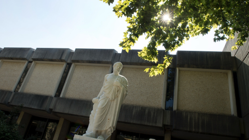 The sun shines through trees above a sculpture of Hippocrates outside the Robert Wood Johnson Medical School on Busch campus.