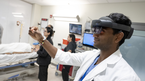 Researcher in a hospital room wearing magnifying eyewear and looking at their hand