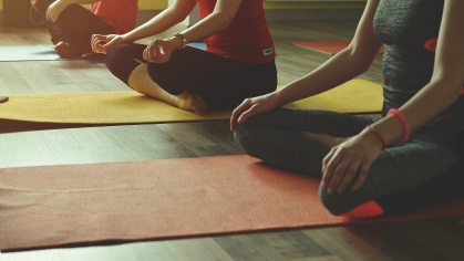 Three people sit cross-legged on yoga mats while meditating