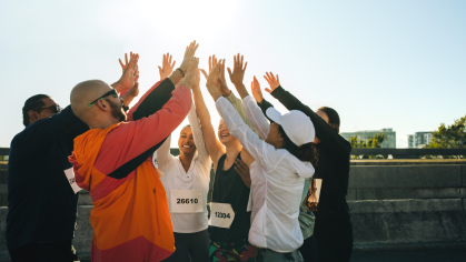 A group of runners raise their hands and high-five in celebration at a race.