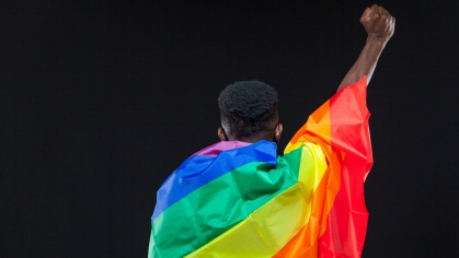 A person holds a rainbow flag and raises their fist 