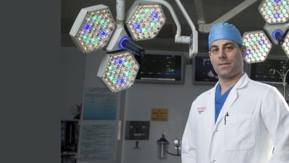 A Rutgers Health doctor wearing a white coat and blue cap stands in an operating room