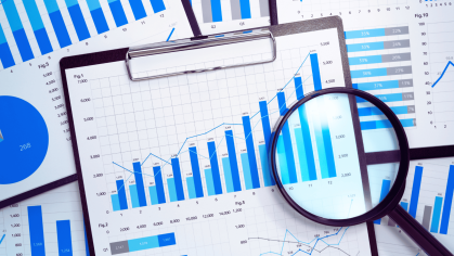 Scattered clipboards with papers full of different graphs and a magnifying glass
