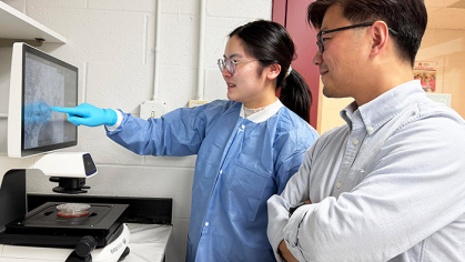 A woman and a man in a lab study a computer monitor with data.