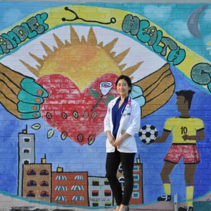 A physician stands in front of a mural in the community