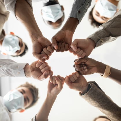 Below view of young diverse group of people in protective medical masks making fist bump standing in circle.