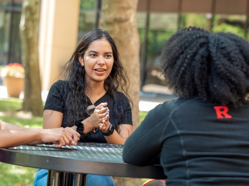 School of Health Professions students and sit and talk at an outdoor table on the Newark campus