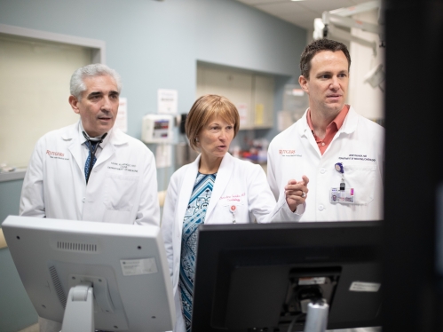 Three doctors look at charts on screens in a medical facility