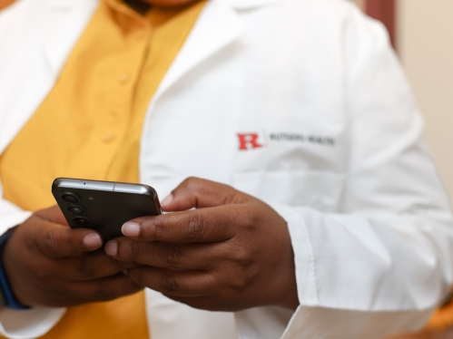 A close-up photo of a person wearing a white lab coat typing on a cell phone