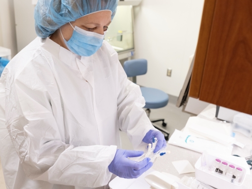 A person wearing scrubs and a hairnet works in the clinical research center.