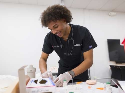 A nursing student in black scrubs practices clinical skills in a lab.