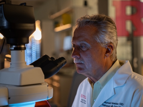 Asthma researcher Reynold Panettieri looks into a microscope in a lab.