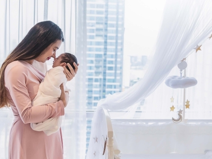 Women holds baby by a window.