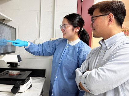 A woman and a man in a lab study a computer monitor with data.