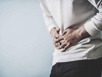 torso of a person in a white shirt clasping hands over stomach, as if in pain