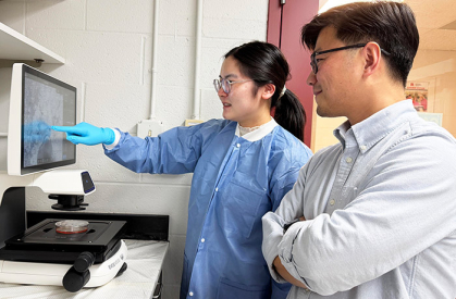 A woman and a man in a lab study a computer monitor with data.