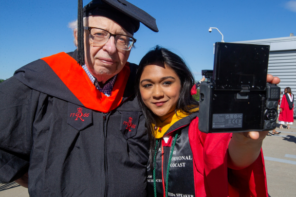 A younger graduating student taking a selfie with an older graduating student