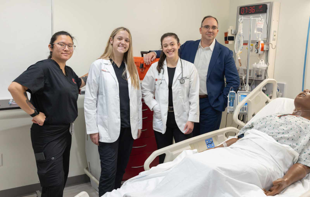 Aj Rose (left), Alex Bell, Amanda Sallemi and Les Barta smile for the camera in a simulation lab at the Ernest Mario School of Pharmacy.
