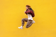 A student jumps in the air against a yellow wall background